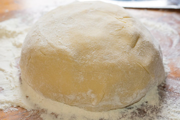 Preparation sweet dough for cookies, pies, cakes. Wad of dough in flour on a wooden table in the kitchen closeup.