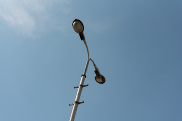 Old industrial street lamp against blue sky with white clouds.