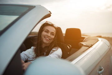 Overjoyed young attractive woman is sitting in luxury car with open roof while enjoying weekend....