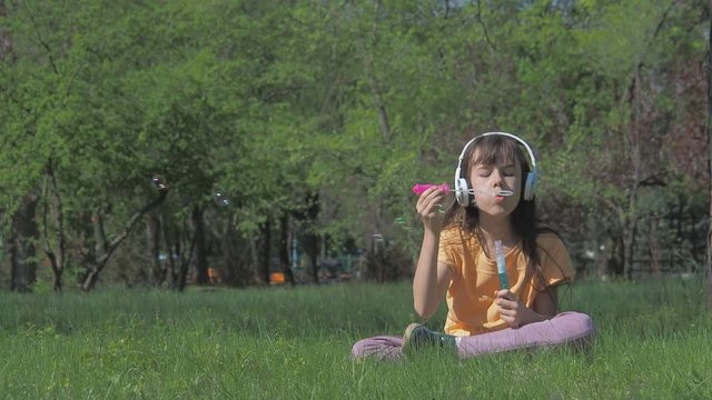 Happy little girl listening to music. A child in a park with soap bubbles.