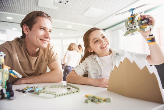 Portrait of cheerful man and glad child playing with modern helicopter while communicating