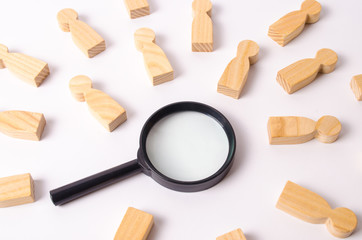 Wooden figures of people lie around a magnifying glass on a white background. Hiring for work, tracing people. The concept of the search for people and workers, human resources.