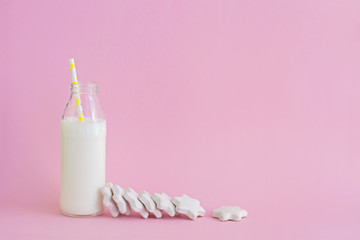 Bottle of milk and cookies shaped stars on pink background