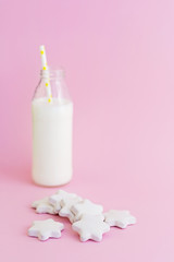 Bottle of milk and cookies shaped stars on pink background