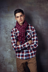 Obraz na płótnie Canvas Portrait of young trendy handsome man with short dark hair wearing checkered shirt and brown trousers standing and posing against gray concrete wall