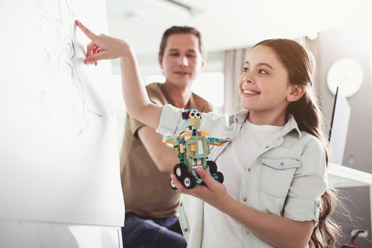 Positive girl pointing at board with image while keeping robot in hands. Modern education concept