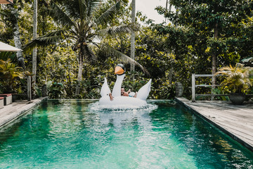 .Young and attractive tourist enjoying a morning in the pool of his hotel in Bali, Indonesia. Using a float shaped like a unicorn. Lifestyle