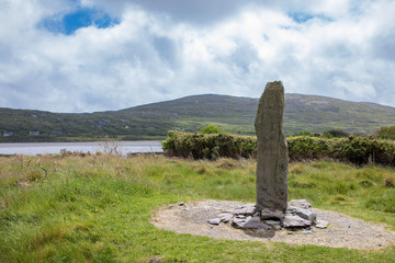 Ogham Stone in Irish Landscape Under Cloudy Blue Sky. Dating for around the 4th century, Ogham is the earliest form of writing in Ireland and was used for around 500 years