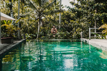 .Young and attractive tourist enjoying a morning in the pool of his hotel in Bali, Indonesia. Jumping and having fun. Lifestyle