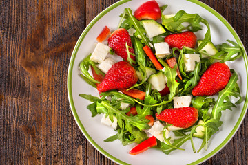 Fresh vegetable strawberry salad on white plate on natural rustic desk.