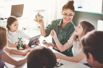 Positive teacher holding modern helicopter. Glad girl controlling it with help of digital device. Toys of future concept