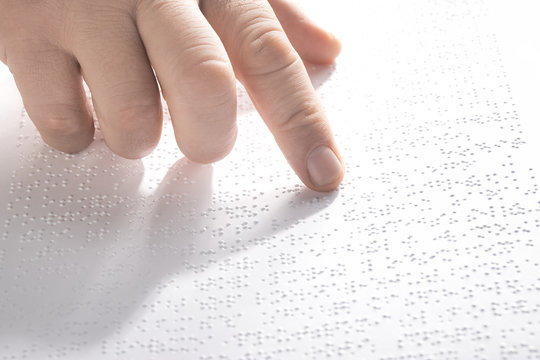 Hand of a blind person reading some braille text touching the relief.