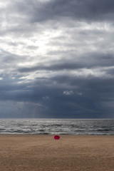Fototapeta na wymiar Single parasol at beach against ocean and thunderstorm