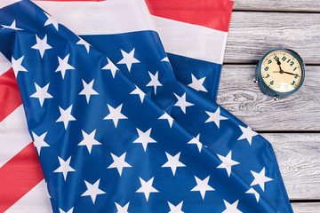 USA flag and mechanical alarm clock. National flag of America and blue alarm clock on old wooden background.Time for patriotic pride.