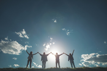 Fototapeta na wymiar Freedom. Full length of four friends holding hands while greeting bright sun in nature. They are standing in line with arms up full of energy and youth spirit 