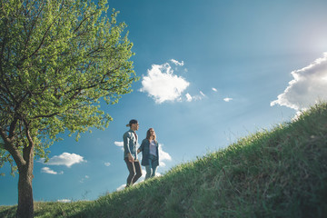 Low angle full length of affectionate girl and boy holding hands and climbing on top of green hill. They are enjoying amazing fresh air and pictorial nature around