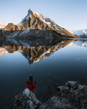 Woman sitting on a rock overlooking a mountain lake with reflection at sunset