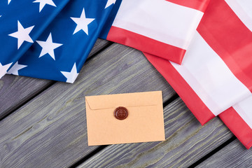 Fototapeta na wymiar American flag and craft envelope. USA flag and vintage style envelope with red wax seal stamp on wooden boards, top view.