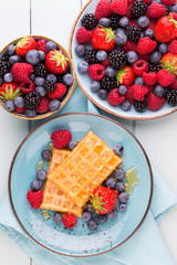 Homemade waffles with berries salad on blue dishes. Vintage wooden background.