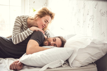Smiling woman is gently embracing partner while he is sleeping. They are staying on comfortable cot during morning time. Girlfriend is enjoying being close to her beloved male