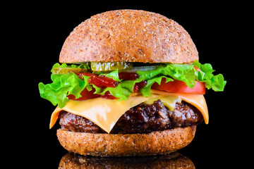 Big tasty hamburger or cheeseburger on black background with grilled meat, cheese, tomato, bacon, onion. Burger closeup