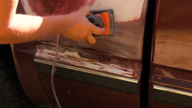 Man using a palm sander sanding a truck