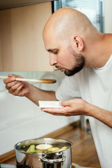 Fototapeta na wymiar man tastes a delicious and fragrant broth from a spoon in the kitchen