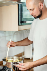man mixes the delicious and fragrant broth in a pot on the gas stove in the kitchen