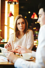 Confident woman and her male colleague sitting in cafe and sharing tablet computer to discuss data on it.