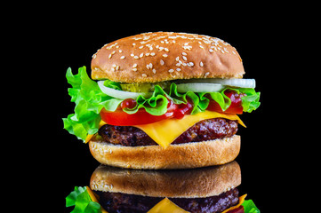 Big tasty hamburger or cheeseburger on black background with grilled meat, cheese, tomato, bacon, onion. Burger closeup
