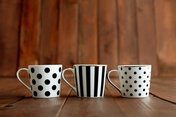 three white-black cups for coffee or tea on a brown wooden floor