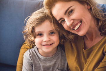 Portrait of happy family looking at camera and smiling indoors. Parent is tenderly bonding her child expressing mother care. Mother and child together concept