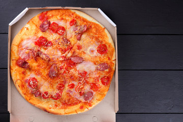 Pizza on a black wooden background, Italian pizza with tomatoes, bacon, sausages and cheese, fast food, festive food on a dark background, copy space