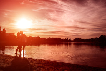 Young couple in love hugging and kissing on summer river bank at sunset. Man and woman having a date