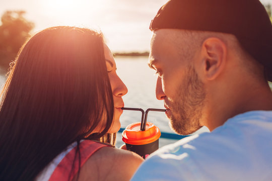 Happy Couple In Love Drinking Coffee Together With A Straw By The River At Sunset