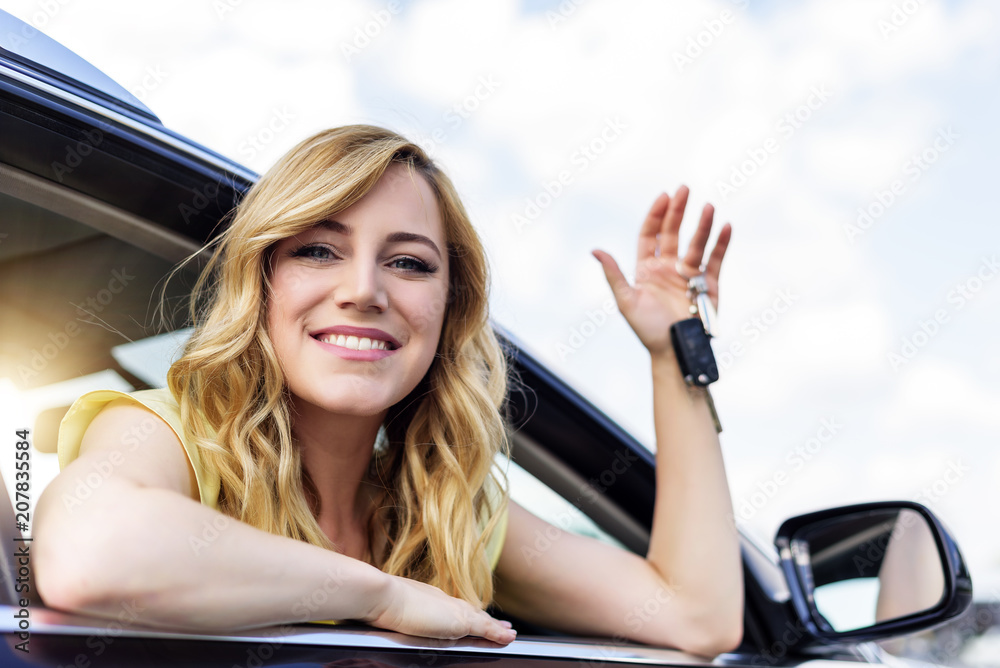 Wall mural An attractive woman in a car holds a car key in her hand.