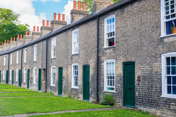 Row of restored Victorian brick houses with green colored doors on a local road in Cambridge, UK