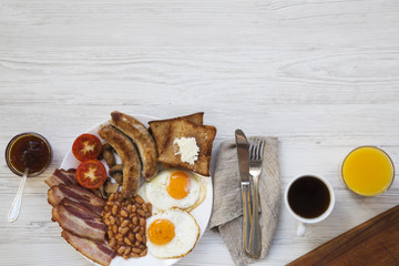 Flat lay of full english breakfast with fried eggs, sausages, bacon, beans and toasts on white wooden background. Top view. Copy space, text area.