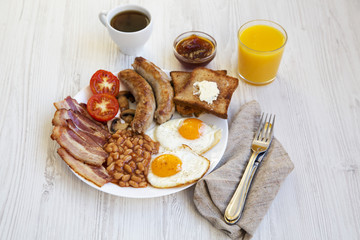 Side view, full english breakfast with fried eggs, sausages, bacon, beans and toasts. White wooden background. Close-up.