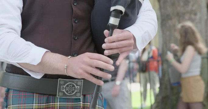 Hands of a bagpipes player in Parliament Square as traffic drives past.