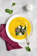 Pumpkin creamy soup with sauteed spinach and blue cheese in a white bowl .Top view.