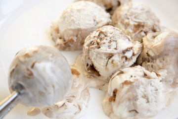 Caramel ice cream in white round plate with spoon for ice cream, close-up.