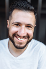 Fototapeta premium Portrait of a stylish hipster Guy, in a white blank t-shirt, on a black fence background, can be used for advertising, text insertion