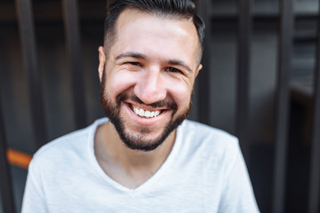 Fototapeta premium Portrait of a stylish hipster Guy, in a white blank t-shirt, on a black fence background, can be used for advertising, text insertion
