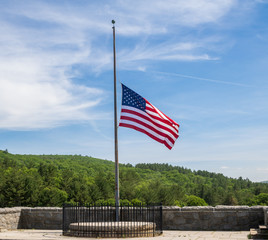 American flag at half staff against a blue sky with cirrus clouds