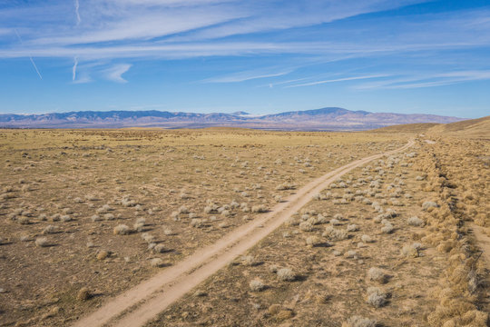 Overhead view of dirt road running alongside a wire fence in the vast dry plains of central California.
