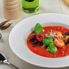 Excellent soup made of tomato and seafood on a rustic wooden table. Plate of healthy Italian meal.