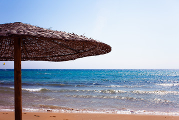 Thatched Straw Umbrellas on a beautiful sandy beach in Corfu Greece. Seashore pleasant view. Seaside clear blue water. Summer vacation time. Relaxation in chair and umbrella