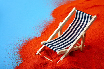 summertime relaxation, minimalism and summer vacation concept with close up on a recliner or deck chair on orange sand against a minimalist blue background with copy space