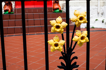Forged yellow items on gate. Decorative fragment in the form of a flower. Metal gate decorations with bright flowers of steel. Beautiful processing metallic flower.